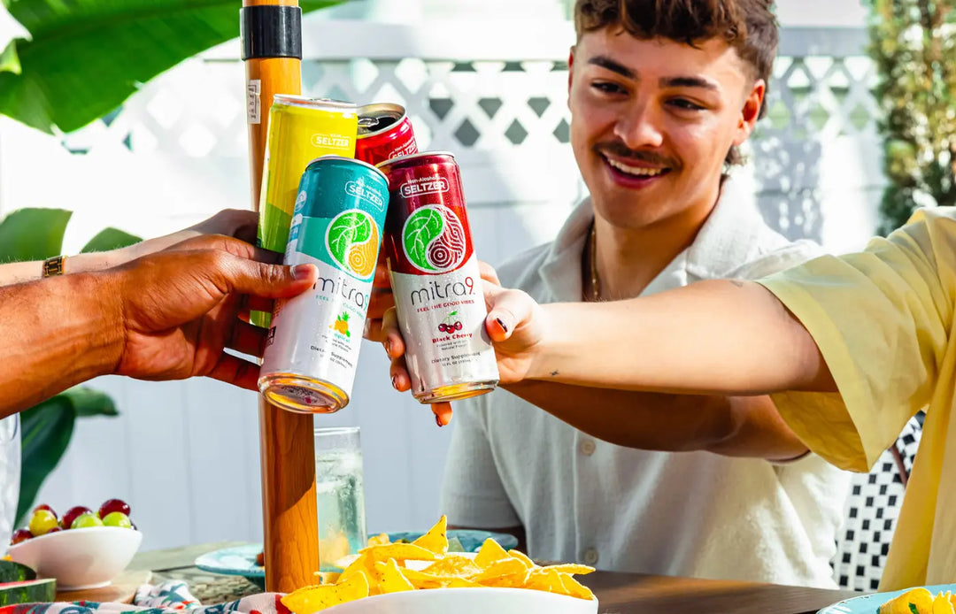 Friends toasting Mitra9 functional drink kava soda cans at outdoor gathering with snacks, showcasing refreshing non-alcoholic seltzer for social relaxation and good vibes