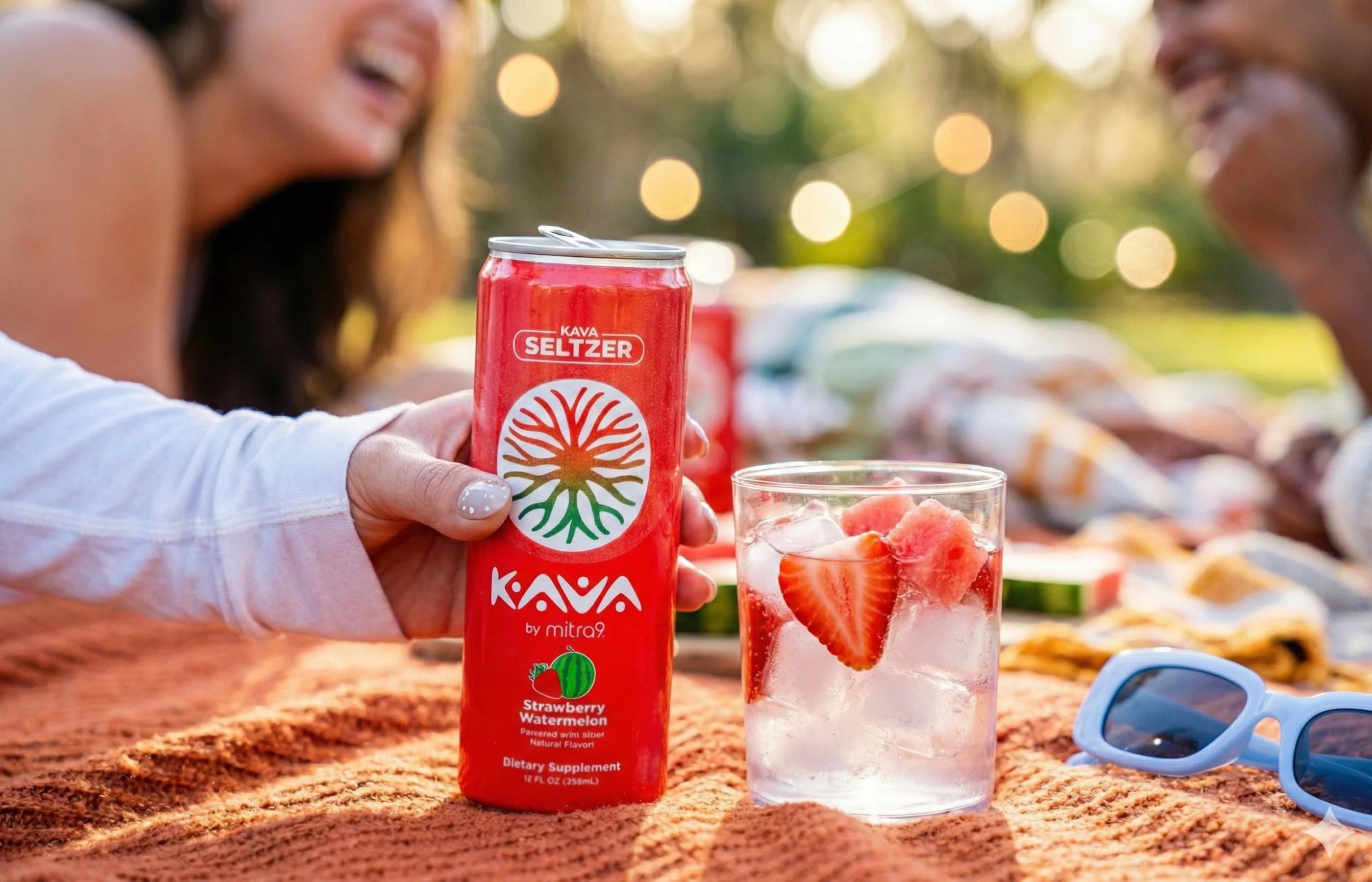 Mitra9 Kava seltzer strawberry watermelon can beside a fruit-infused drink at a sunny outdoor picnic with friends enjoying a non-alcoholic beverage