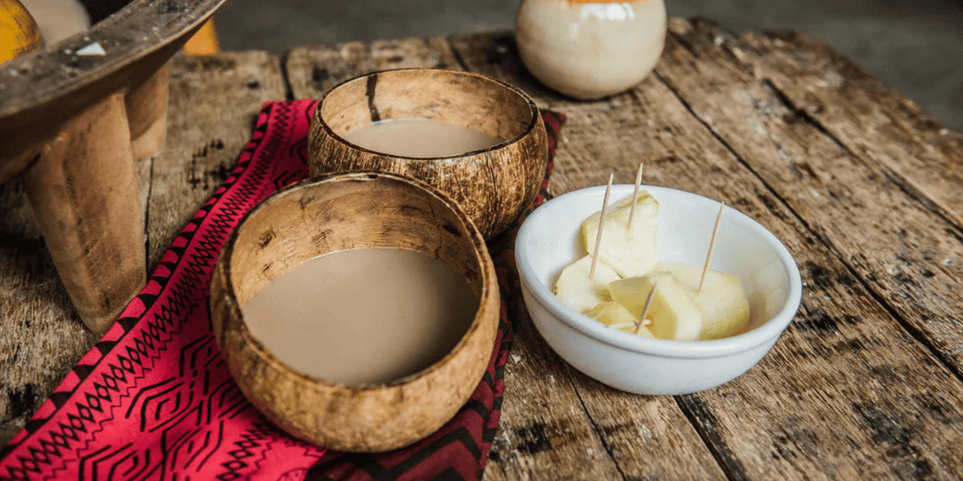 Coconut bowls filled with traditional Kava on a wooden table, served alongside fruit pieces, representing Pacific Island Kava rituals