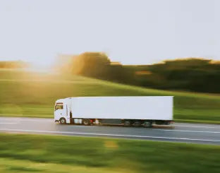 White truck driving on a road with greenery in the background